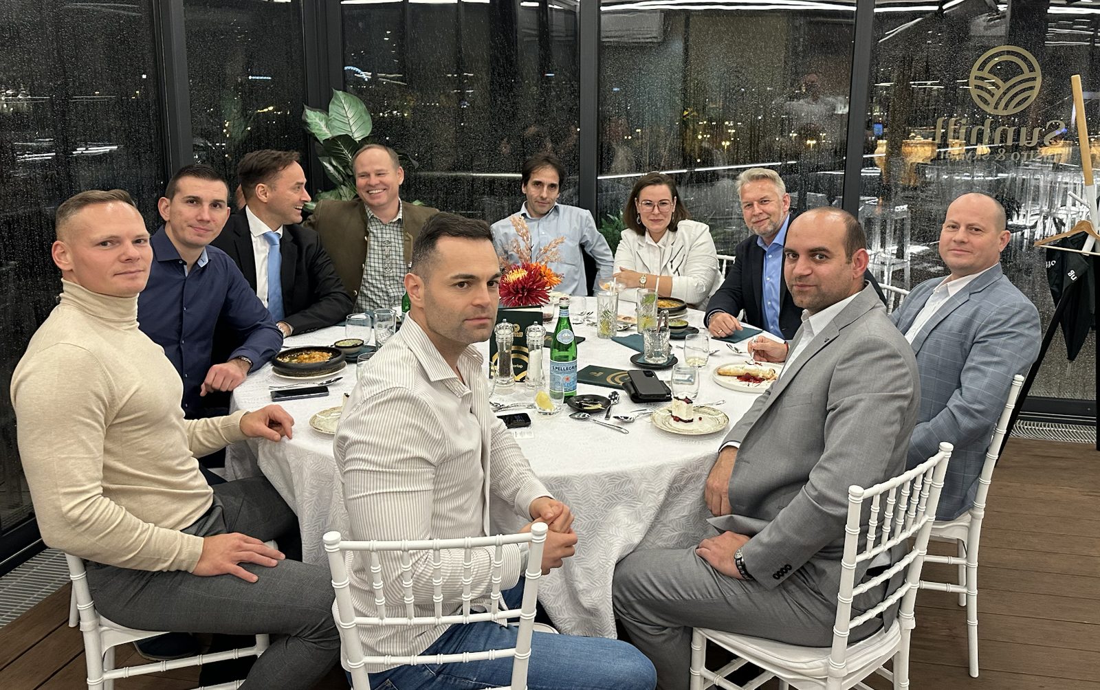 Vacsora résztvevői egy kerek asztalnál a Sunhill Bistro & Skybar üvegfalú Skybar részén